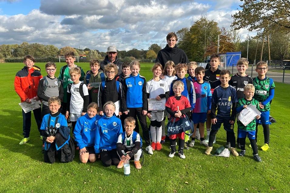 Gruppenshot von Kindern in Sportkleidung auf einem Fu&szlig;ballfeld, l&auml;chelnd und posierend f&uuml;r das Foto.