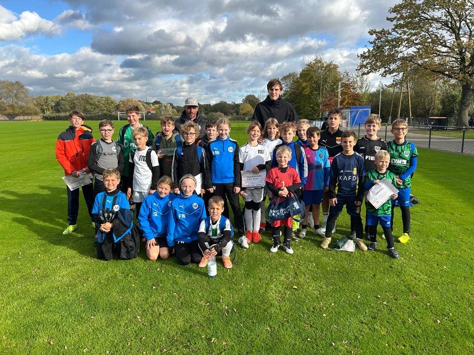Gruppenshot von Kindern in Sportkleidung auf einem Fu&szlig;ballfeld, l&auml;chelnd und posierend f&uuml;r das Foto.