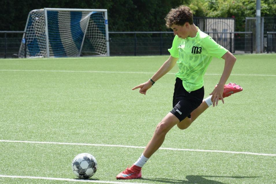 Jugendlicher in neongr&uuml;ner Sportbekleidung tritt einen Fu&szlig;ball auf einem Kunstrasenplatz. Im Hintergrund das Tor.